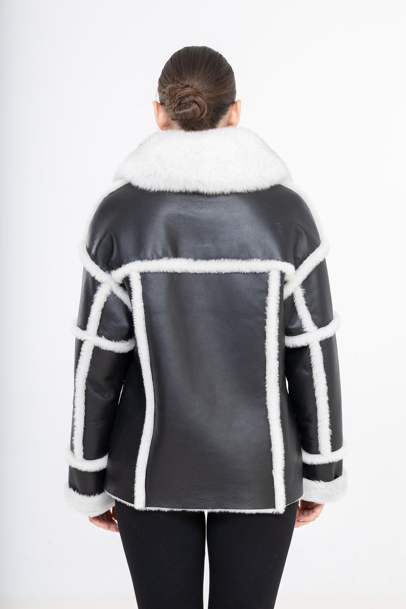 Black leather shearling jacket with white shearling trim worn by a person on a white background